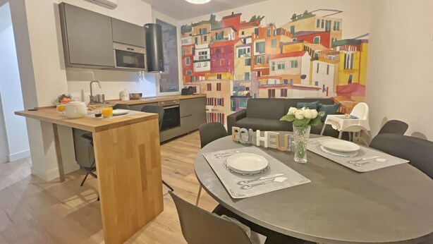 A modern kitchen with a wooden island, a dining table set with plates and cutlery, and a colorful mural on the wall. - Happy Family Apartments Soziglia (Genoa)