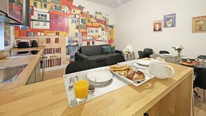 A modern kitchen with a dining area, a colorful mural on the wall, and a bar counter with breakfast items. - Happy Family Apartments Soziglia (Genoa)