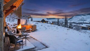 Eine Holzhütte mit Kamin, Sitzgelegenheit im Freien und verschneiter Landschaft im Hintergrund.
