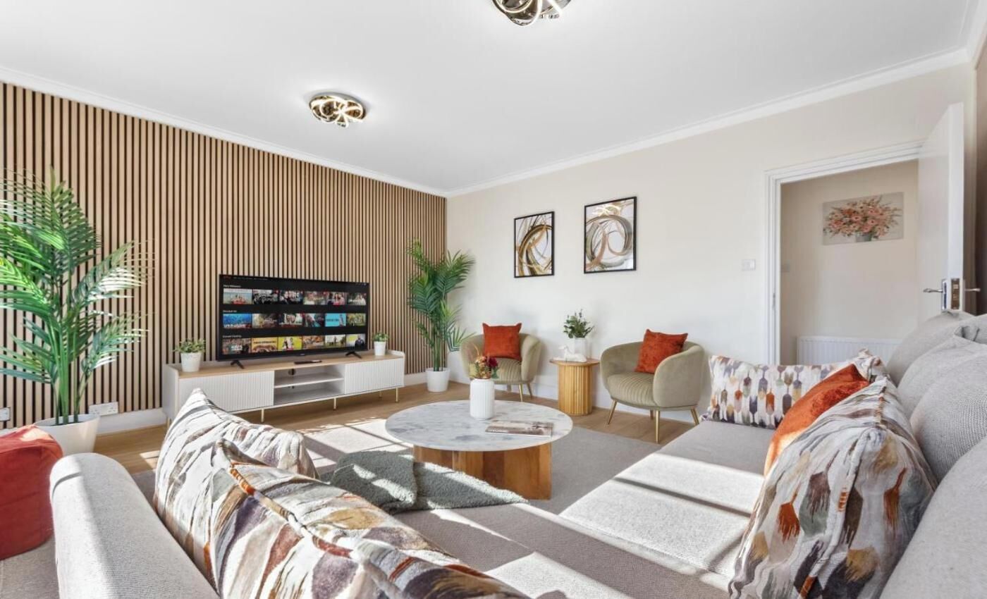 Ein modernes Wohnzimmer mit einer Couch, einem Couchtisch und einem Fernseher. An den Wänden befinden sich Pflanzen und Kunstwerke.