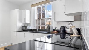 Een moderne keuken met witte kasten, een groot raam en roestvrijstalen apparatuur.