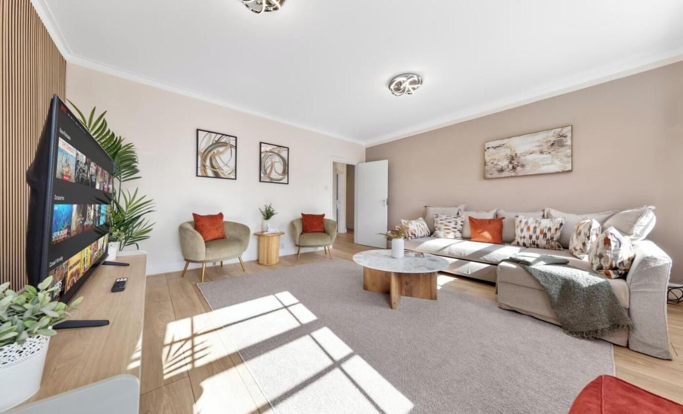 Ein modernes Wohnzimmer mit einer Couch, Sesseln, einem Couchtisch und einem Flachbildfernseher.