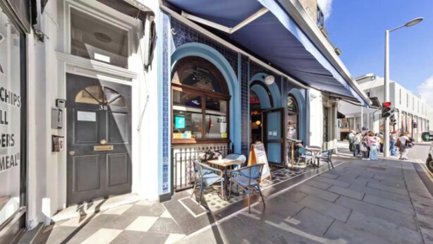 Een restaurant met terras, een blauw luifel en een betegelde stoep.