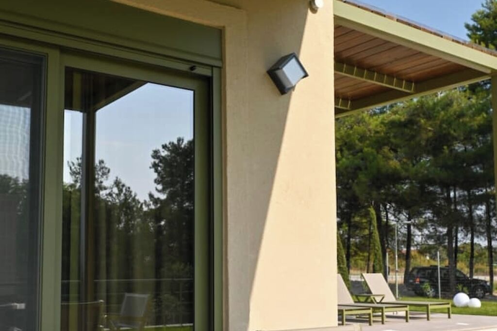 A modern building with large sliding glass doors, a covered outdoor seating area, and a small outdoor TV screen.