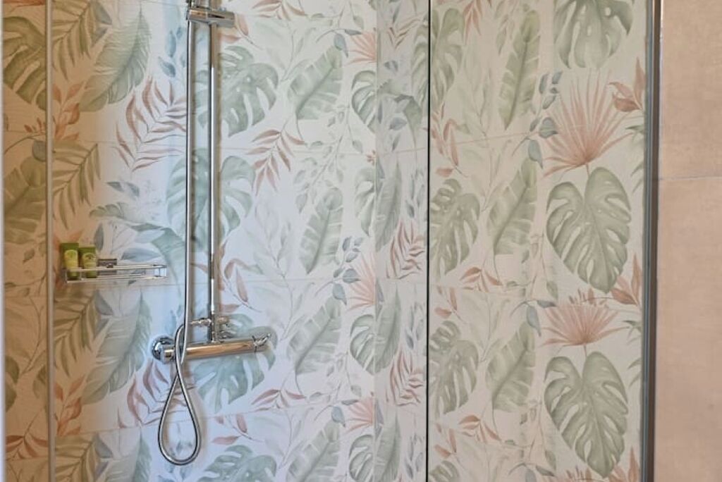 A shower with a glass door, surrounded by a wall with a tropical leaf pattern.