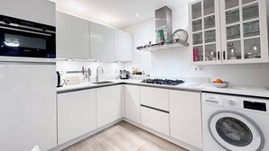 A modern kitchen with white cabinetry, a built-in oven, a gas stove, a sink, and a washing machine.