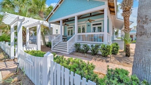 Ein Küstenhaus mit überdachter Veranda, weißem Zaun und einer Palme.