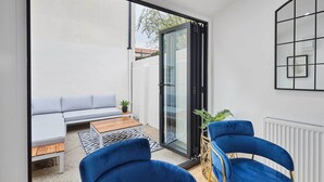 A modern patio with a sliding glass door, a grey sofa, a wooden table, and two blue chairs. - Host & Stay | Ginger Bread Cottage (Stokesley)
