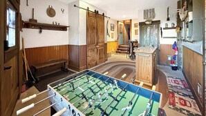 Habitació amb taula de futbolí, mobles de fusta i una escala que condueix a una altra zona.