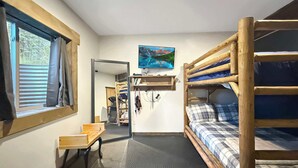 Habitació petita amb lliteres, escriptori, cadira, taula petita i televisió penjada a la paret.