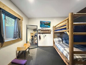 A compact room with bunk beds, a desk, a chair, a small table, and a TV mounted on the wall. - The Tennessee Pass A-frame Cabin — 9 Acres | Mt Elbert Views | Wood Stove | Sleeps 4 (Leadville)