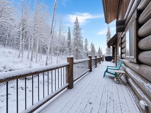 Una terraza de madera con barandillas cubiertas de nieve y un banco, con vistas a un bosque.