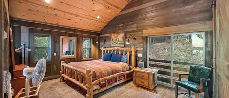 Une chambre confortable dans un chalet, avec un grand lit, un fauteuil, un bureau et une fenêtre donnant sur le paysage extérieur.