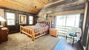 A rustic wooden bedroom with a large bed, a small bedside table, a chair, and a window. - The Tennessee Pass A-frame Cabin — 9 Acres | Mt Elbert Views | Wood Stove | Sleeps 4 (Leadville)