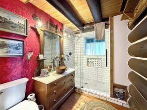 Un baño con tocador de madera, inodoro, lavamanos con espejo y zona de ducha con ventana.