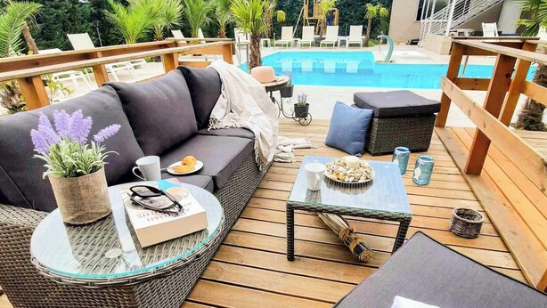 Une terrasse avec un canapé, une petite table et une chaise. On aperçoit une piscine au fond.