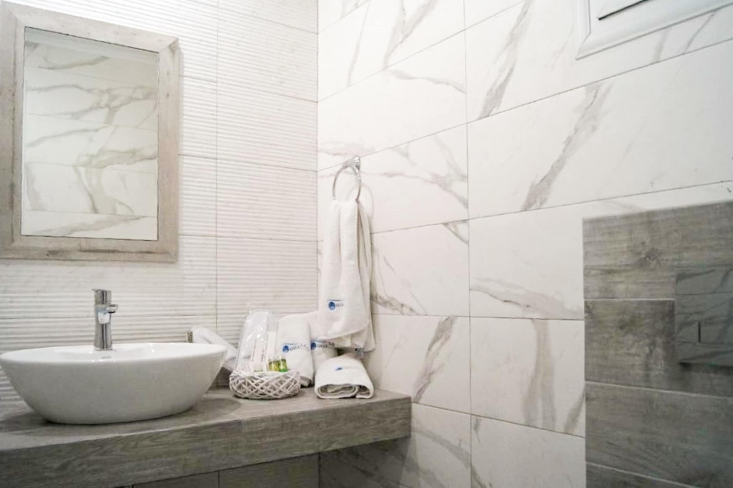A bathroom with a white sink, marble tiles, a towel rack, and a framed artwork on the wall.