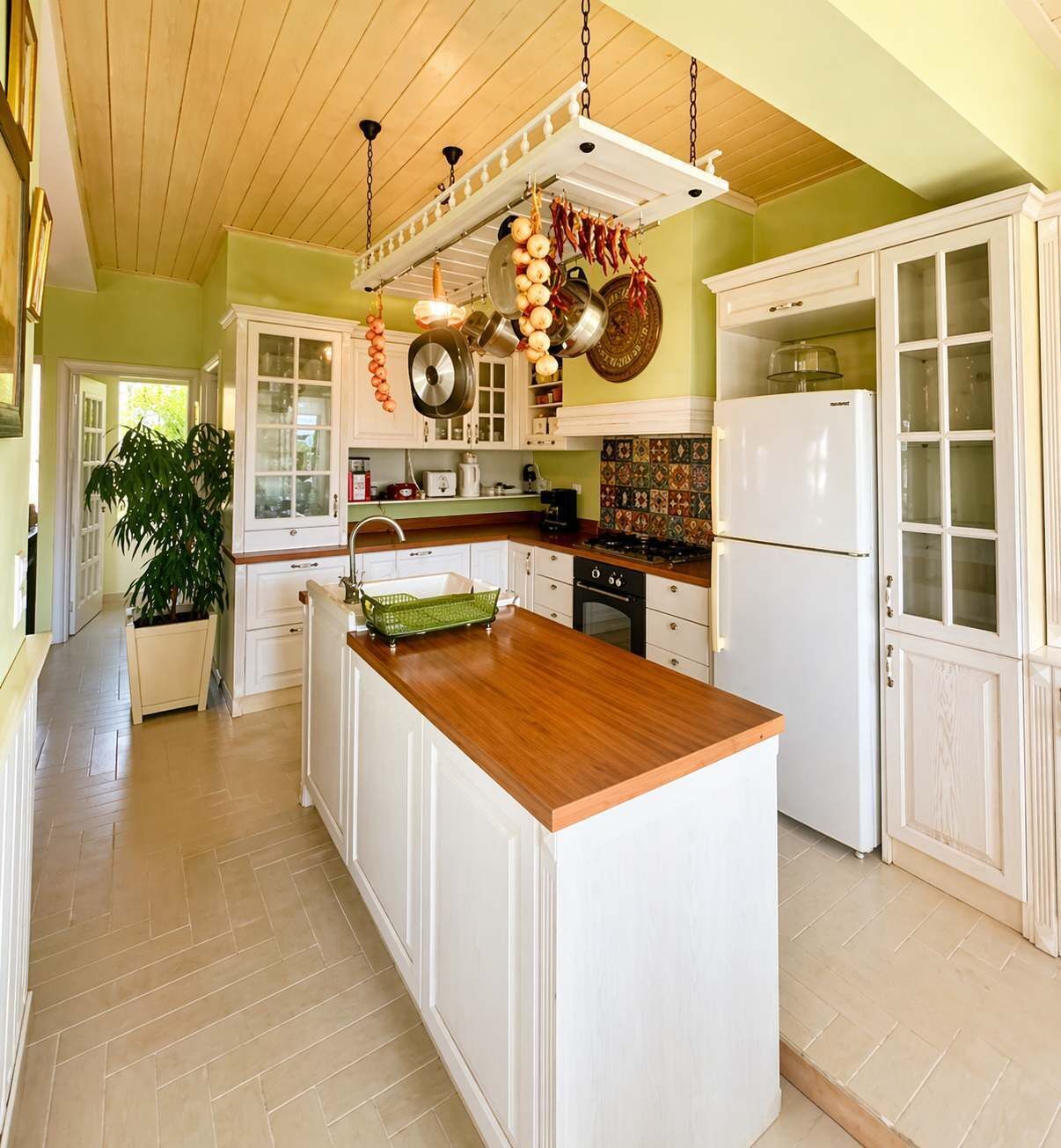 Cucina con mobili bianchi, isola in legno e pentole appese.