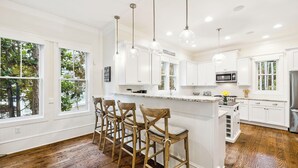 A modern kitchen with white cabinetry, a central island with bar stools, pendant lighting, and a view of greenery outside. - Private Pool and LSV Watercolor Getaway (Santa Rosa Beach)