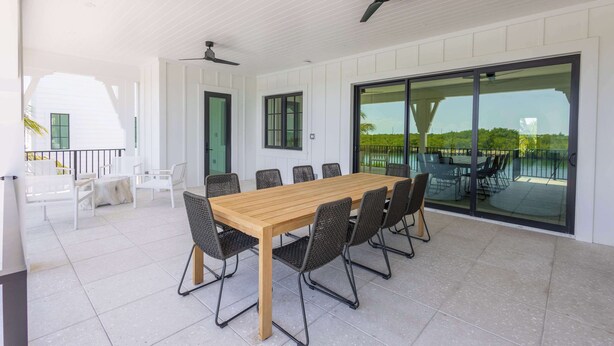 Un patio amplio con mesa y sillas de madera, ventiladores de techo y vistas a través de grandes puertas de cristal.