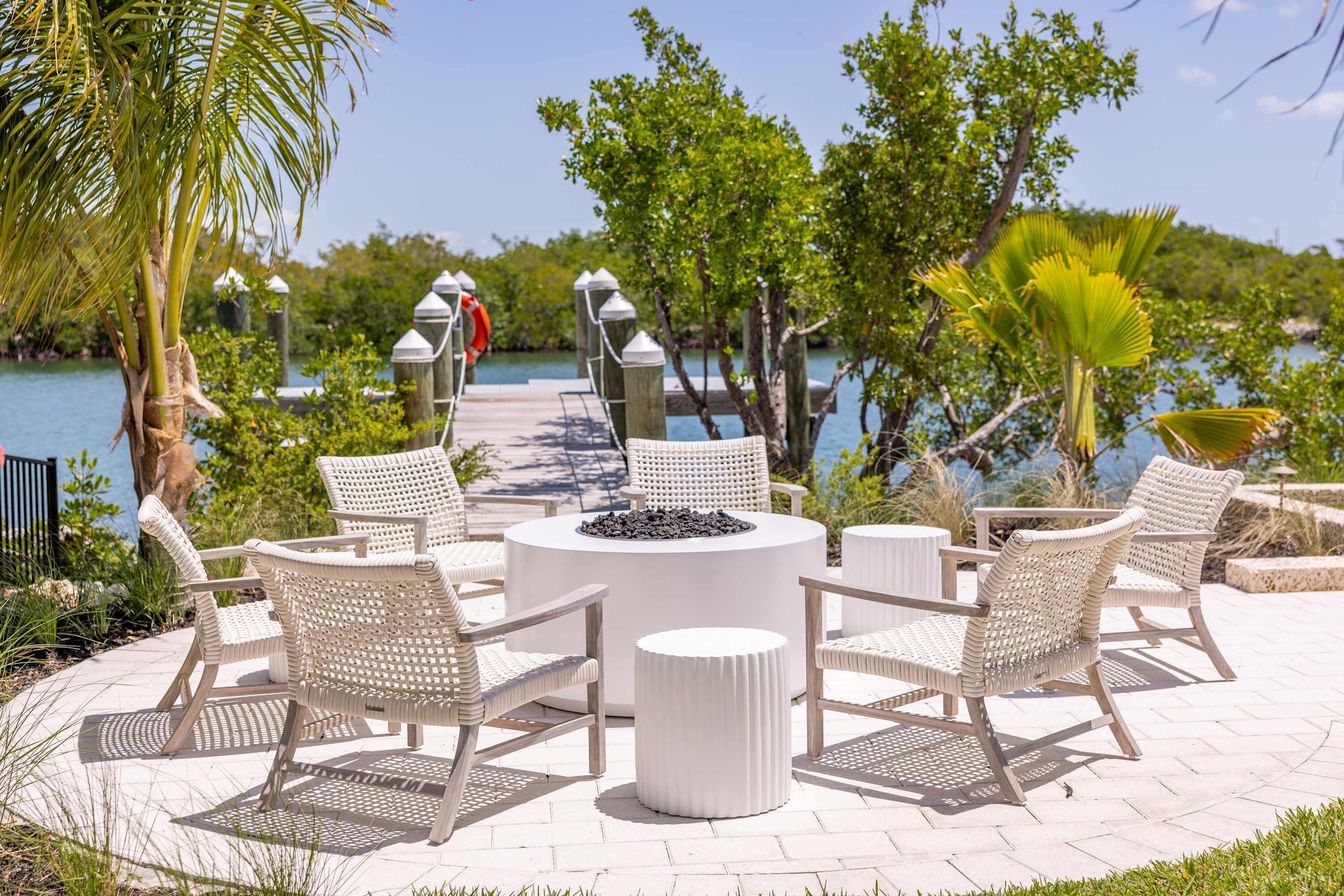 Een terras met rieten stoelen en een ronde tafel, omgeven door groen en uitzicht op het water.