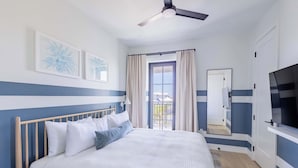 Un dormitorio con cama, ventilador de techo, ventana con cortinas y televisor.