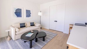 Una sala de estar moderna con un sofá, dos mesitas negras, una lámpara de pie y una obra de arte abstracta en la pared.
