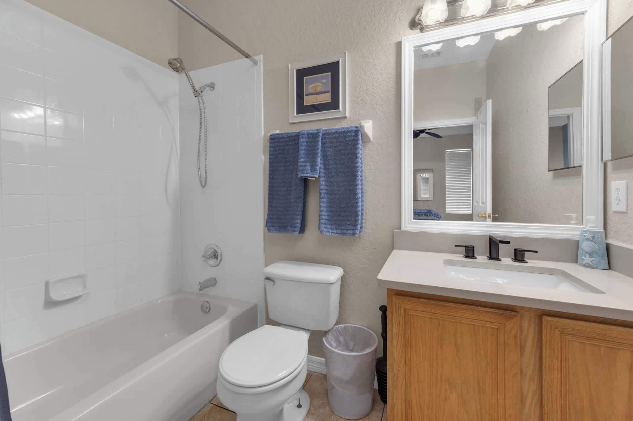A bathroom with a bathtub, toilet, sink, and a mirror with lights.