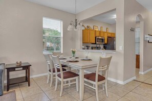 A dining area with a table set for four, a kitchen with wooden cabinets, and a window with blinds.