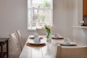 Un coin repas avec une table dressée pour quatre personnes, des assiettes blanches, des tasses et un vase rempli de fleurs.