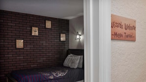 Uma cama de solteiro com um cobertor estampado em um quarto com parede de tijolos e um letreiro que diz 'Wizards Welcome - Muggles Tolerated'.