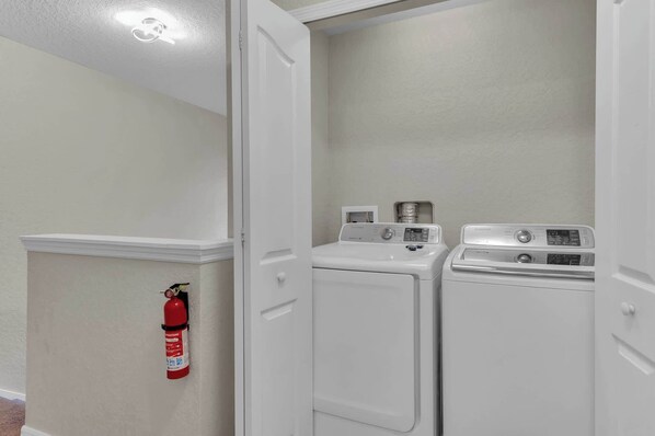 A laundry room with two washing machines and a fire extinguisher mounted on the wall.