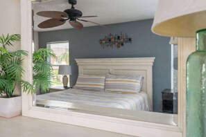 A bedroom with a bed, a ceiling fan, a window, and a wall decoration.