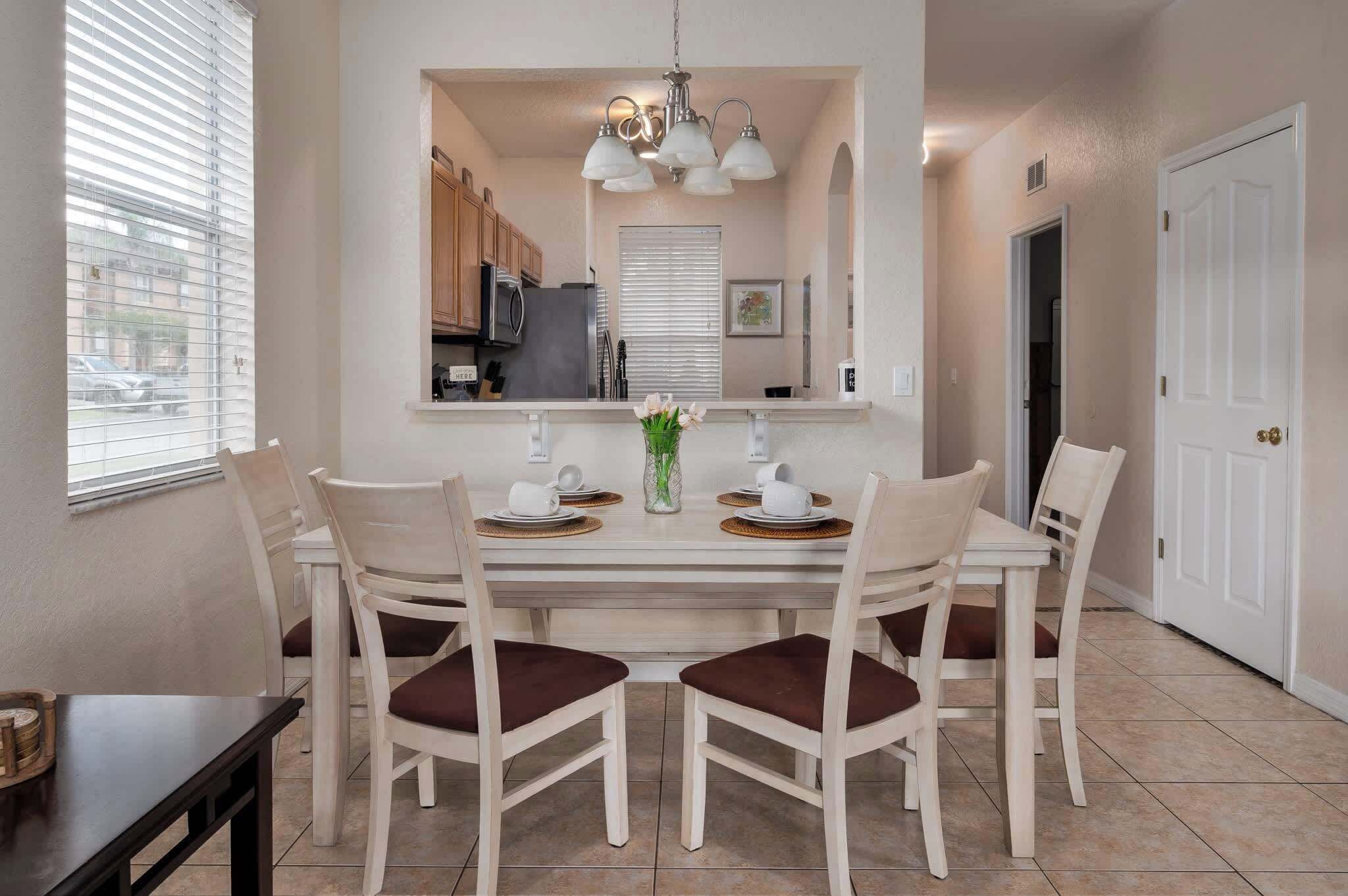 A dining area with a white table, four chairs, and a vase of flowers.