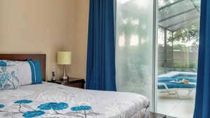 A bedroom with a bed, a nightstand, a lamp, a sliding glass door to a pool area. - Resort Villa w/ Private Pool & Family Fun (Davenport)