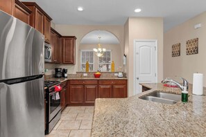 A kitchen with granite countertops, wooden cabinets, a stainless steel refrigerator, a stove, and a sink. - Resort Villa w/ Private Pool & Family Fun (Davenport)