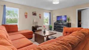A living room with orange sofas, a wooden coffee table, a TV, and a ceiling light fixture. - Resort Villa w/ Private Pool & Family Fun (Davenport)