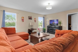 A living room with orange sofas, a wooden coffee table, a TV, and a ceiling light fixture.