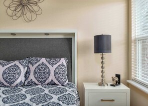 A bedroom with a patterned bedspread, a bedside lamp, a decorative wall piece, and a window with blinds. - Resort Villa w/ Private Pool & Family Fun (Davenport)