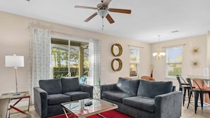 A living room with two grey sofas, a glass coffee table, a red rug, a ceiling fan, and a dining area with a table and chairs. - Resort Villa w/ Private Pool & Family Fun (Davenport)