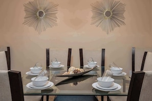 A dining table with a central serving dish, surrounded by white bowls and saucers, set against a wall with decorative sunburst mirrors.