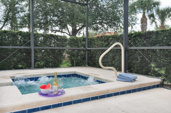 A hot tub with a bottle of champagne, a glass, and a bowl of watermelon slices.