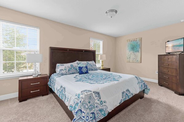 A bedroom with a large bed, two bedside tables, a dresser, and a ceiling light.
