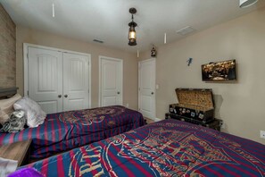 A bedroom with two beds, a chest of drawers, a television, and a wall-mounted picture.