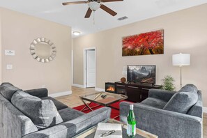 A living room with a ceiling fan, a fireplace, a television, and a red rug. - Resort Villa w/ Private Pool & Family Fun (Davenport)