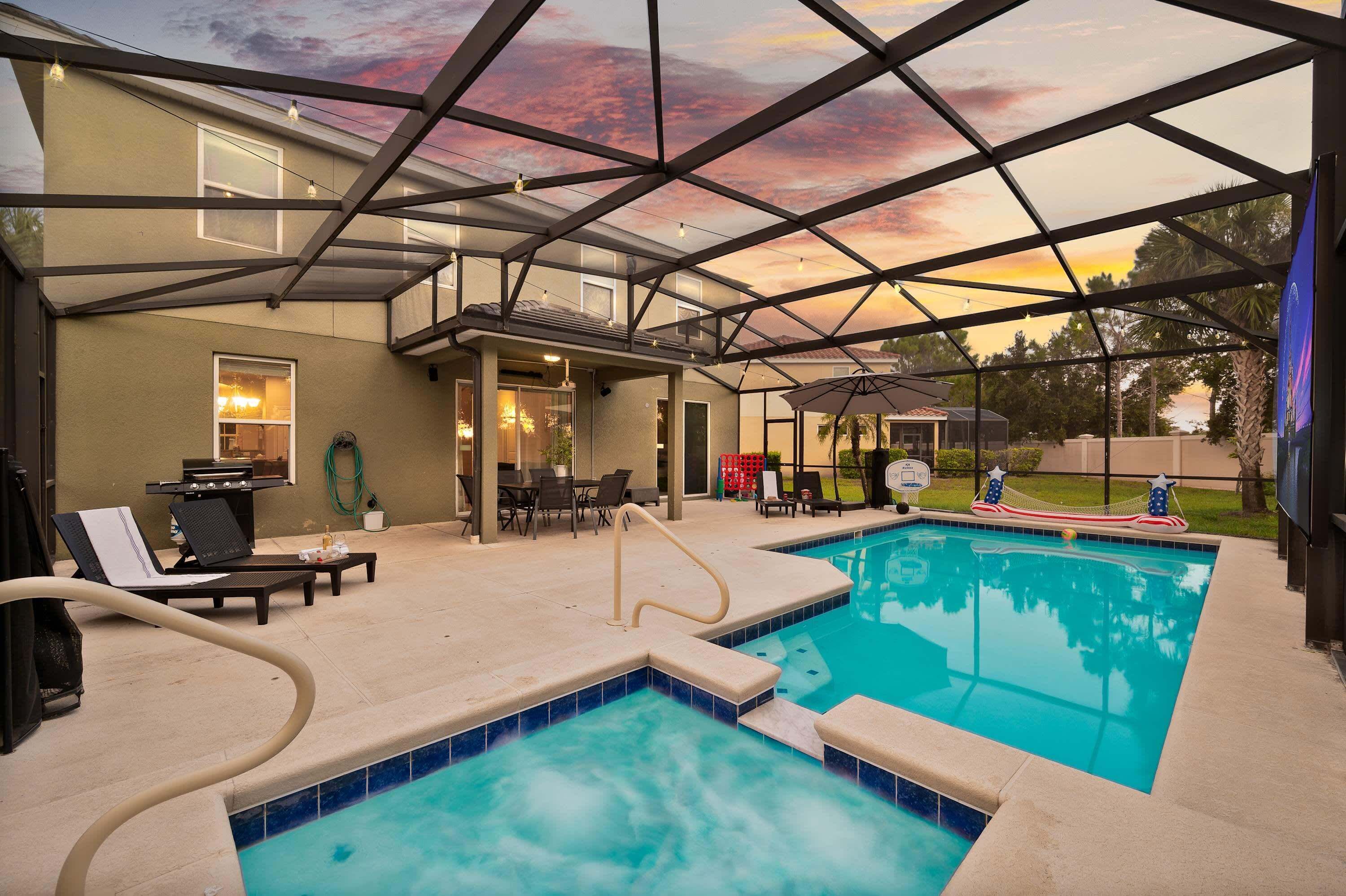 Ein überdachter Pool mit Liegestühlen, einer Grillgegend und Blick auf den Sonnenuntergang.