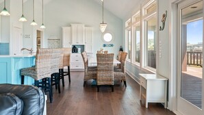 A spacious kitchen with white cabinets, a dining area with wicker chairs, and a view of the outside. - Sunset Bliss 4 Bedroom Home (Port Bolivar)