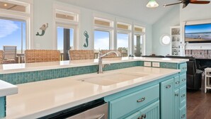 A kitchen with a large island, teal cabinetry, and a view of the ocean through large windows. - Sunset Bliss 4 Bedroom Home (Port Bolivar)