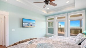 A bedroom with a large bed, a ceiling fan, and a view of the beach through the windows. - Sunset Bliss 4 Bedroom Home (Port Bolivar)