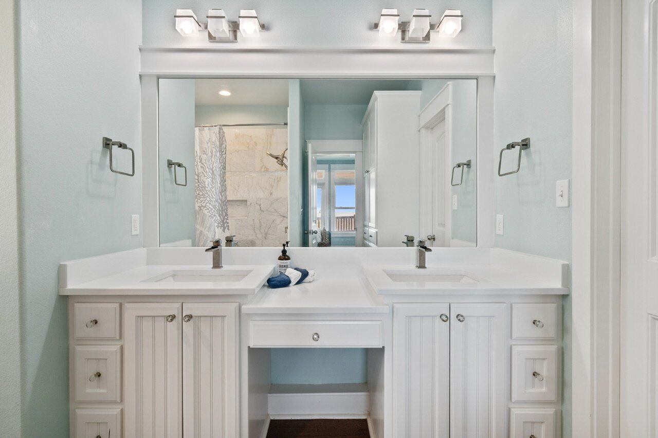A bathroom with two sinks, a large mirror, and a shower with a marble wall.